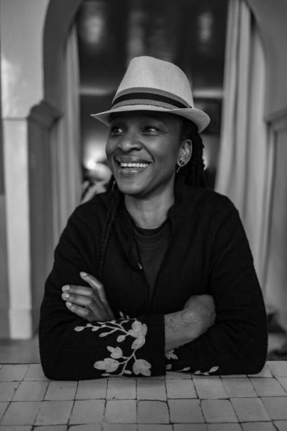 black-and-white image of author Chika Unigwe, wearing hat and smiling.